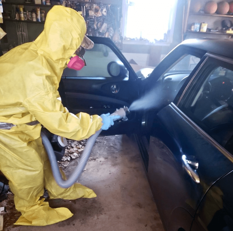Man in yellow suit decontaminating a car of covid-19
